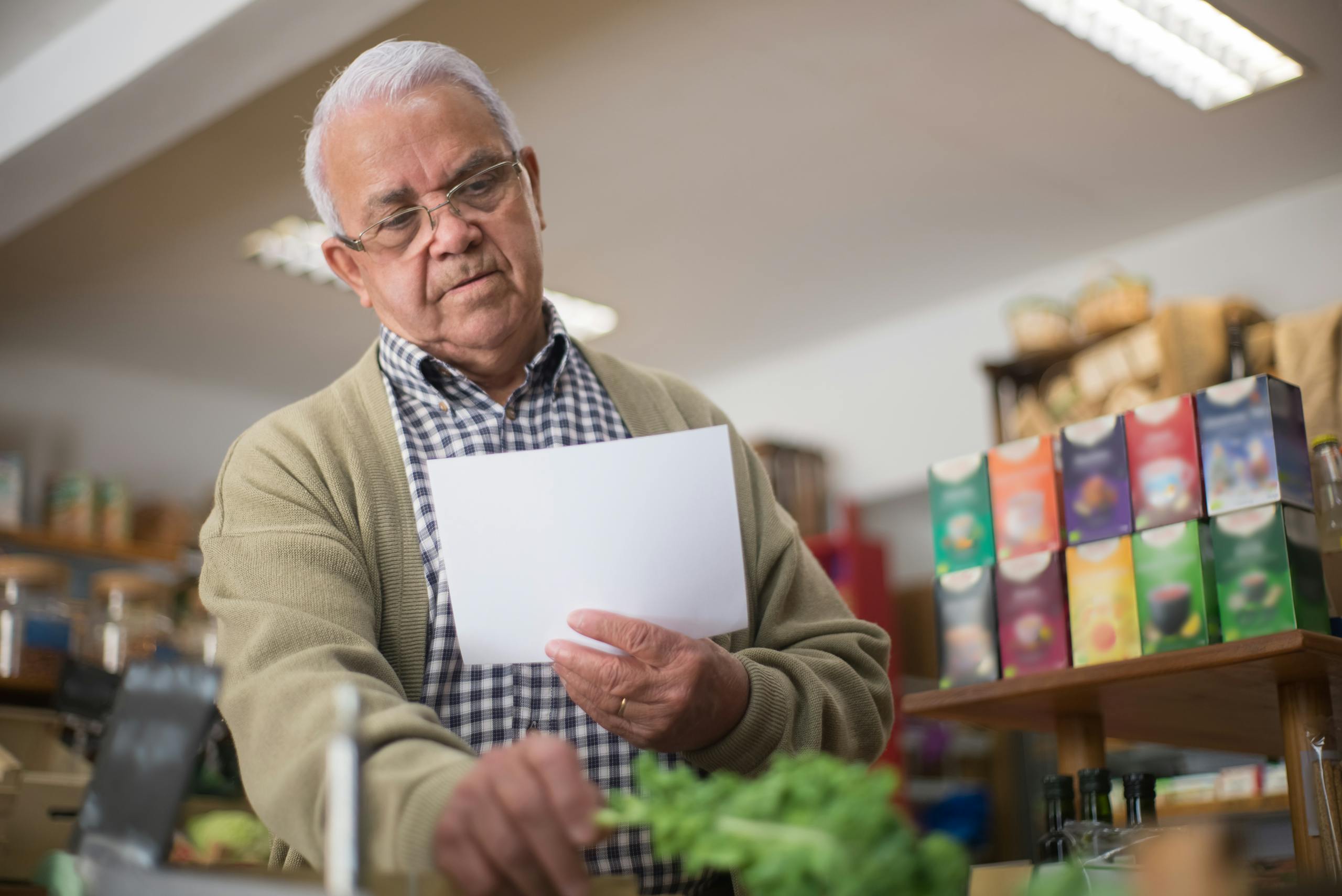 Elderly man shopping in a Portuguese grocery store, holding a paper list.